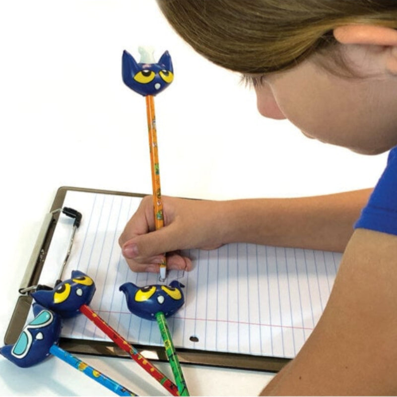A child writing in a notebook with a blue cat-shaped pencil topper and matching pencil guards, shown in a close-up lifestyle shot.