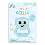 A Glo Pals Light-Up Rattle toy in its original packaging, featuring a light blue cartoon monster rattle with a white belly and large black eyes on a light blue backing card.