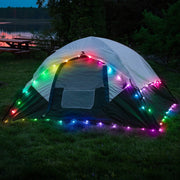 Tent decorated with colorful string lights in camping setting by lake
