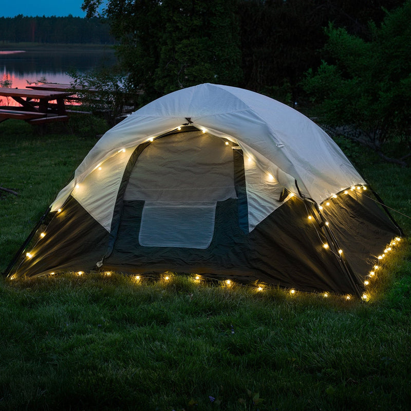 Illuminated tent with warm white globe string lights in lakeside camping setting at dusk