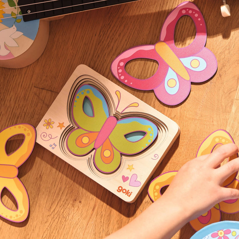 Colorful butterfly-shaped wooden puzzle on a wooden surface with a hand interacting with it.