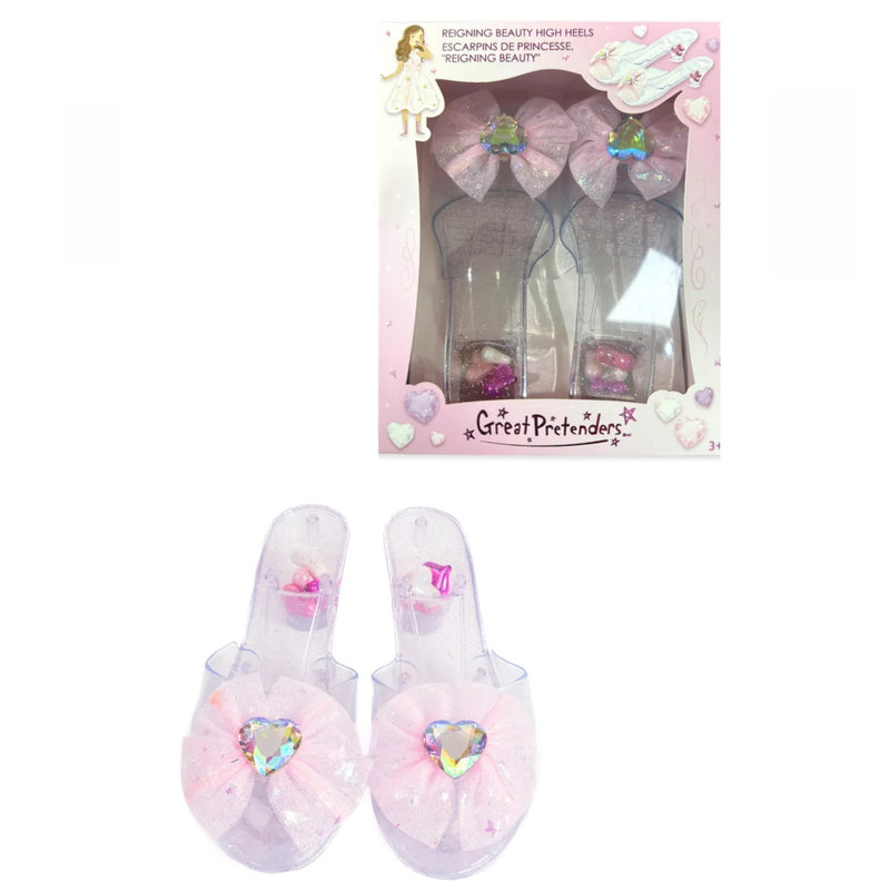 A pair of pink and clear plastic high-heeled slide sandals with large bow and heart embellishments, shown both inside their retail packaging and as a standalone product on a white background.