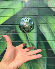 Hand catching metallic blue-green Waboba Moon Ball in mid-air against geometric green background