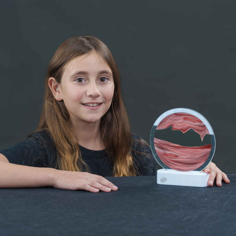 Young girl smiling and displaying circular LED sand art with pink swirled pattern
