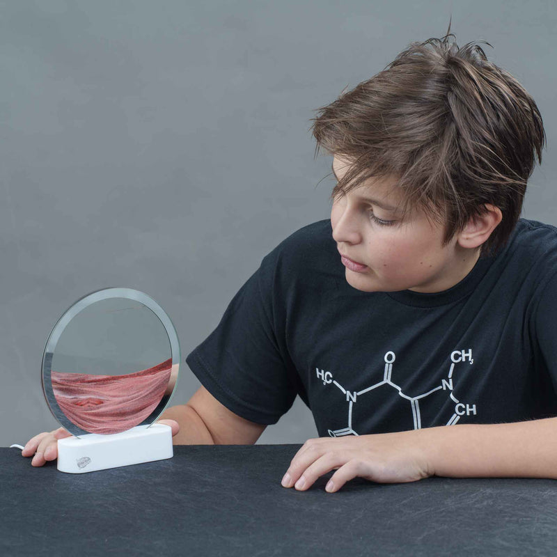 Child examining Lyells Sand Art LED display showing layered sand patterns in circular frame