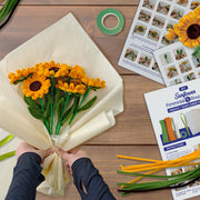 Hands crafting sunflower bouquet with chenille stems and instruction manual on wooden table