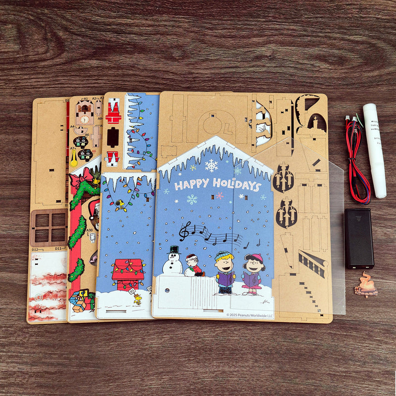 Peanuts Christmas House DIY model kit with wooden pieces, instructions, and electronics on wooden surface