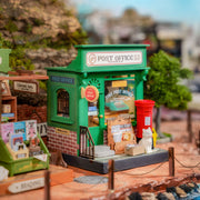 Green miniature post office building model with red mailbox in outdoor setting