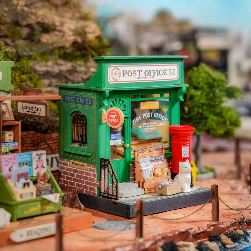 Green miniature post office building model with red mailbox in outdoor setting