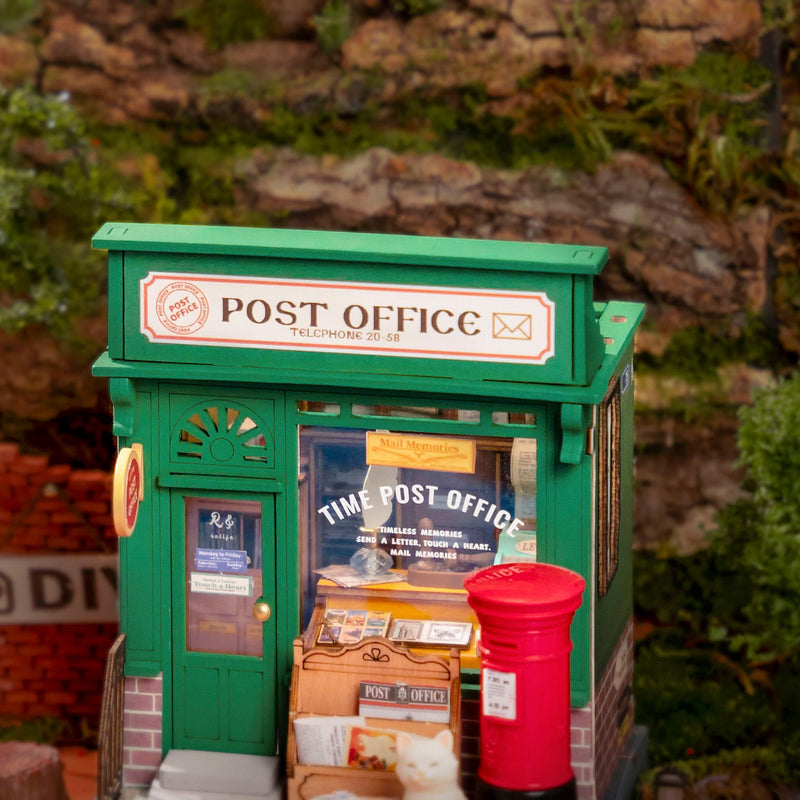 Green miniature post office building with red mailbox in outdoor garden setting