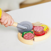 Child's hand using toy pizza cutter on wooden play pizza with colorful toppings