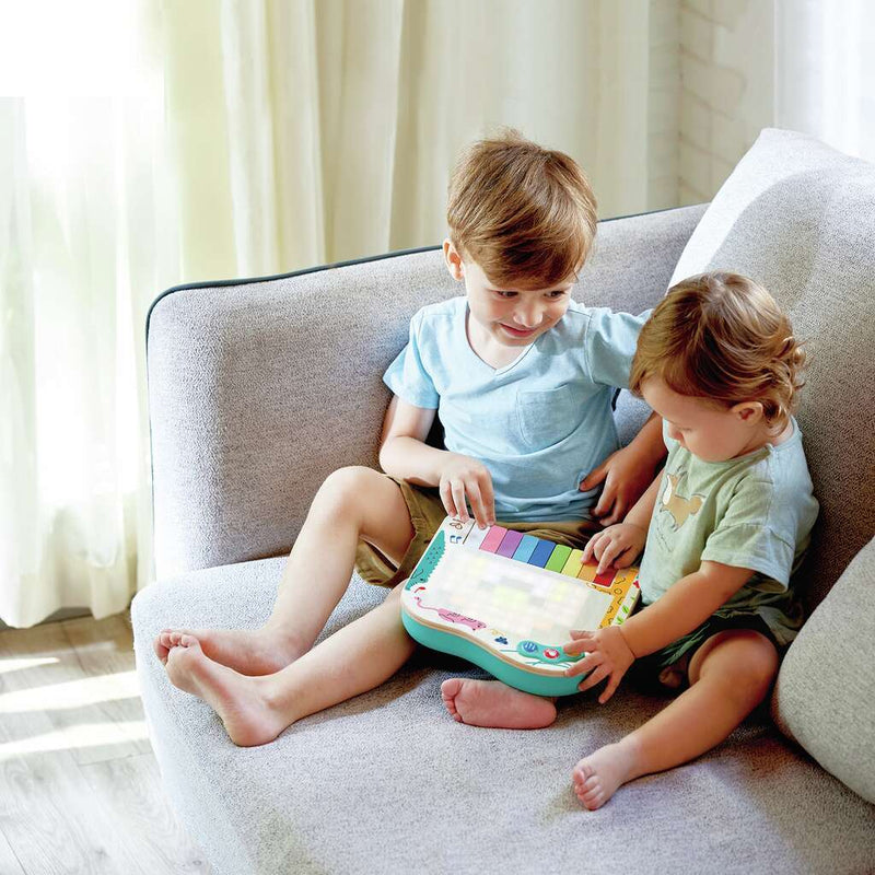 Two young children sitting on sofa playing with Hape Pixel Piano toy together