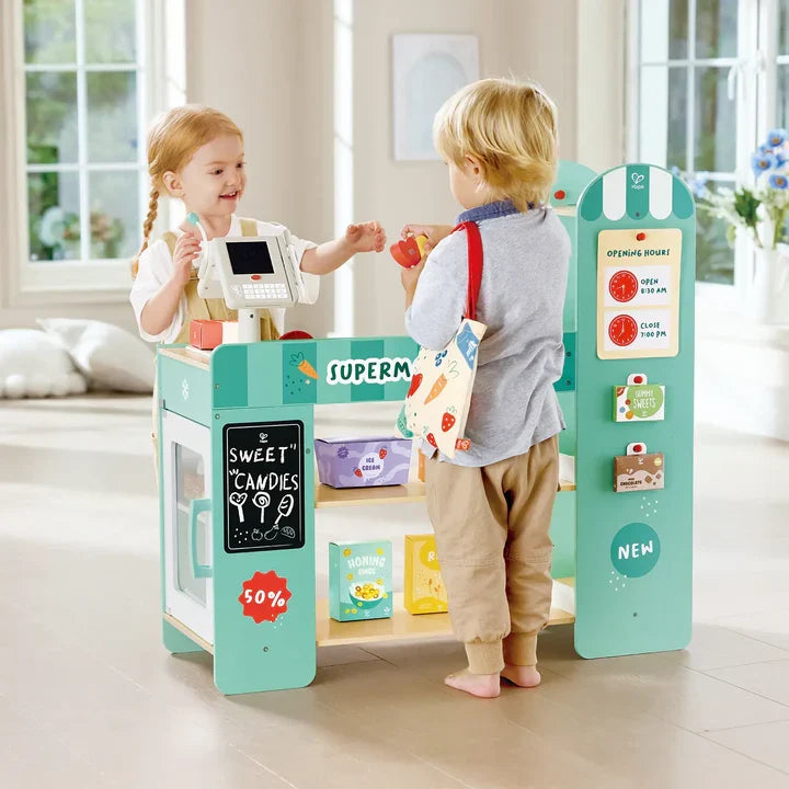 Two children playing with Hape wooden supermarket toy set in bright room