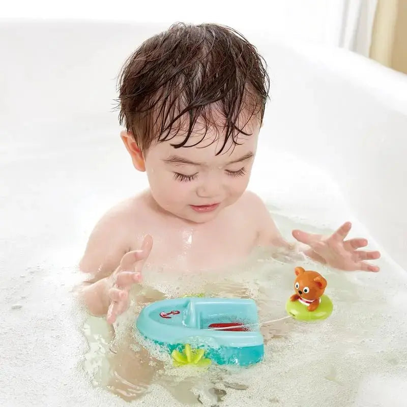 Toddler playing with Hape pull-back boat and bear floatie toy in bathtub