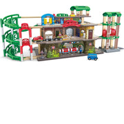 A wooden toy train station and track set with a multi-level station building, green elevated tracks, a garage, small trains, a bus, and a blue car on a white background.