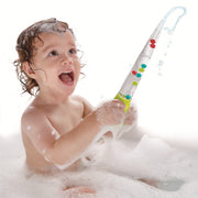 A baby with wet, soapy hair sits in a bubble bath while holding a clear plastic toy shower sprayer with colorful bubbles, creating a shower stream of water and bubbles.