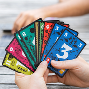 Hand holding a deck of colorful playing cards with numbers and symbols.