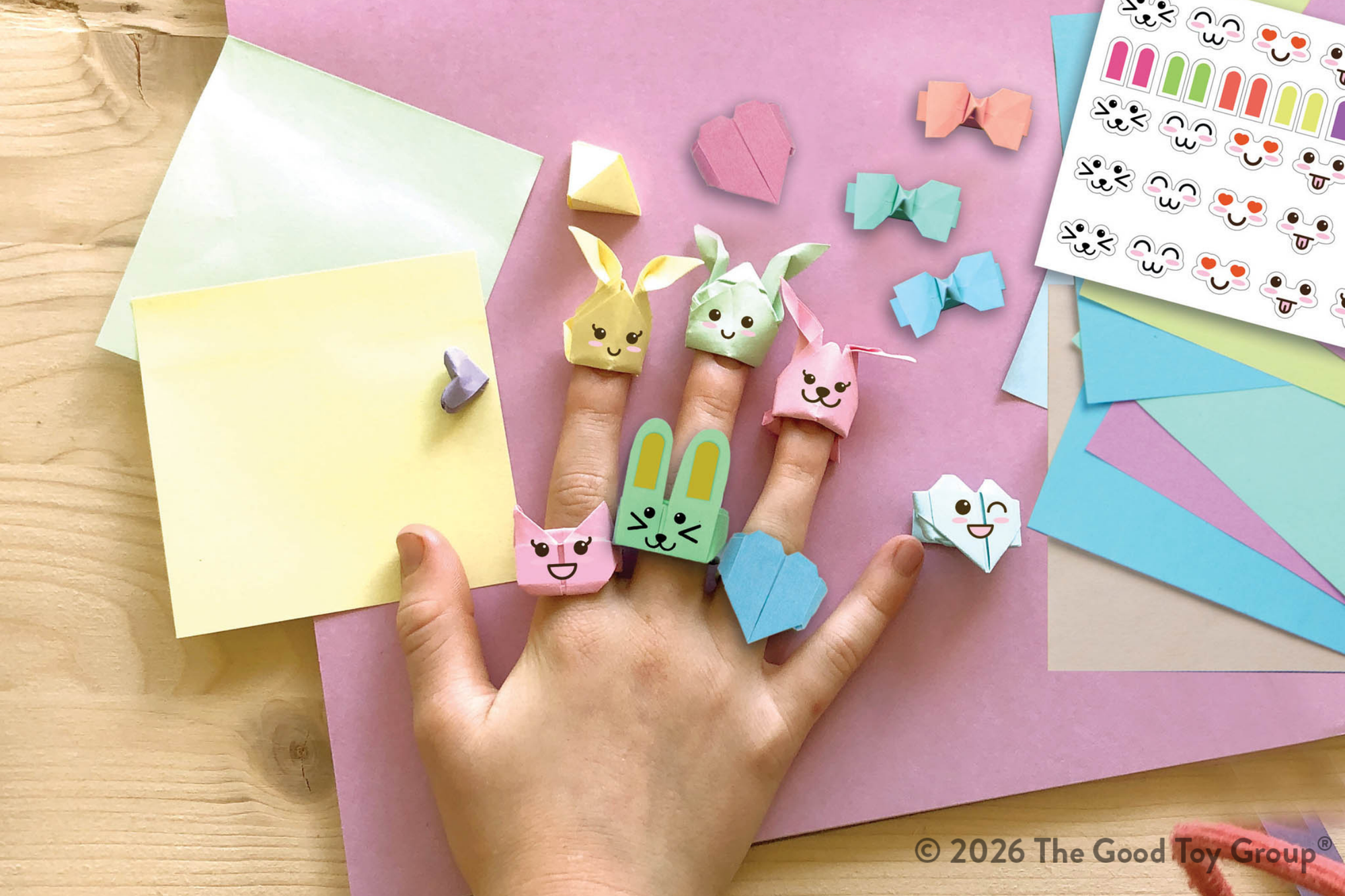 Origami Bunny Finger puppets on a child's hand with colorful paper and stickers on a pink background.