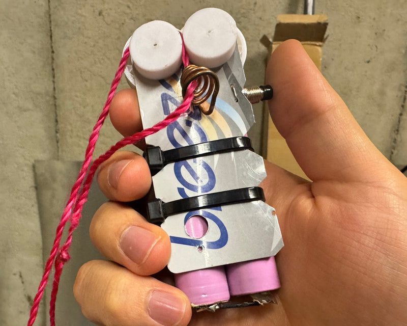Hand holding ZipString device with blue text and pink components connected by red string