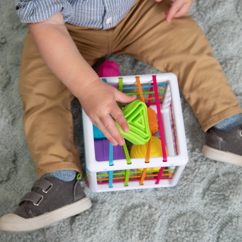 Child playing with Fat Brain's InnyBin shape sorting toy made up of colorful building blocks in a white container on a gray carpet.