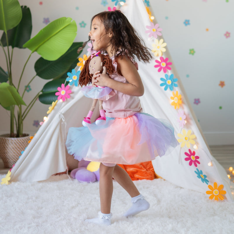 Young girl in rainbow tutu hugging Groovy Girls Iris doll near decorated play teepee