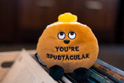 Orange potato plushie with cute face saying You're Spudtacular on wooden surface