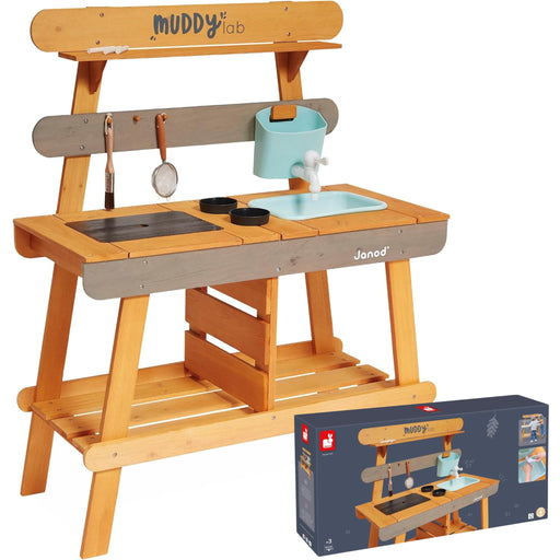 A wooden children's play kitchen set by Janod and Muddy Lab, featuring a natural wood frame, gray front panel, light blue sink and bucket, and toy kitchen accessories. The product is shown alongside its retail packaging box on a plain white background.