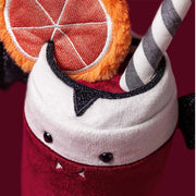 A close-up of a plush Halloween drink cup decoration, featuring a red velvet-like body, white plush whipped cream top, black glitter trim, a striped gray-and-white straw, and an orange slice accent on a dark red background.
