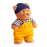 Bartholomew Bear from Jellycat wearing a blue knitted hat, striped shirt, and yellow overalls on a white background.