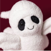 A close-up of Ghost Bob, a plush ghost toy with black embroidered eyes, nose, and mouth, set against a solid dark red background.