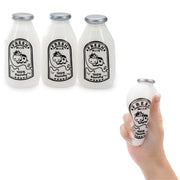 Three small squishy milk bottle-shaped objects are shown on a white background, plus a hand holding one of them. The objects resemble frosted glass milk bottles with silver caps and black cow illustrations with the words 'Fresh Milk' and '100% Squishy.