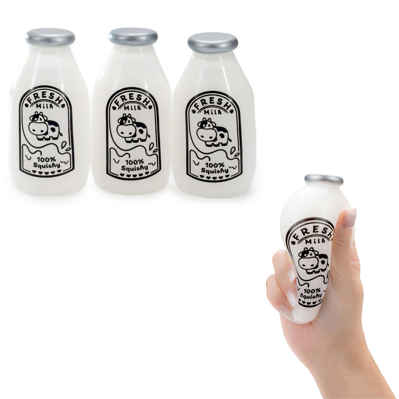 Three small squishy milk bottle-shaped objects are shown on a white background, plus a hand holding one of them. The objects resemble frosted glass milk bottles with silver caps and black cow illustrations with the words 'Fresh Milk' and '100% Squishy.
