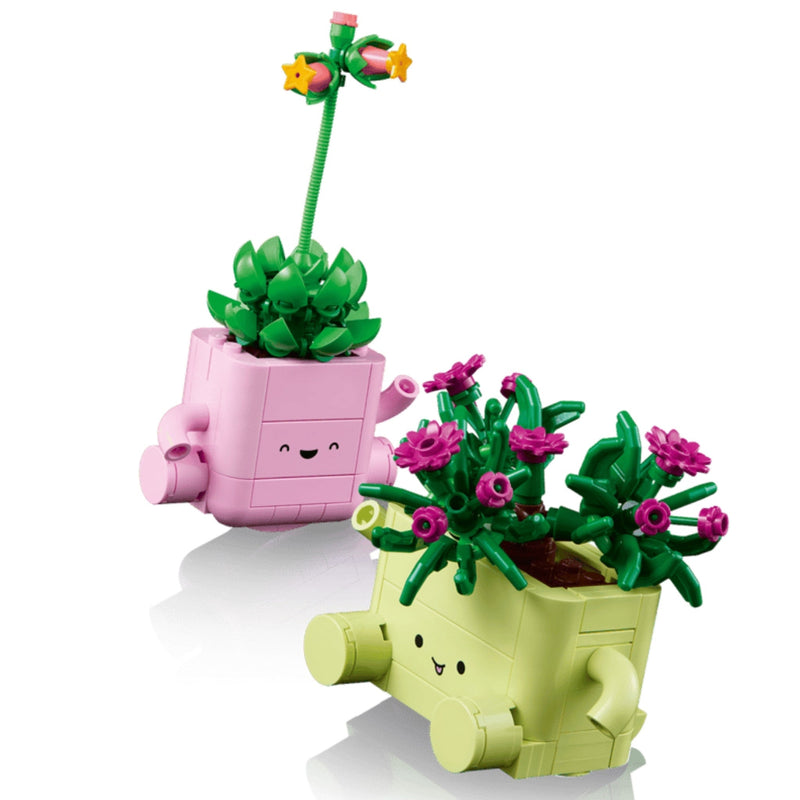 Two cute, block-style planter toys from LEGO on a clean white background. One pink planter holds a green succulent with a long green stem and small yellow flowers.