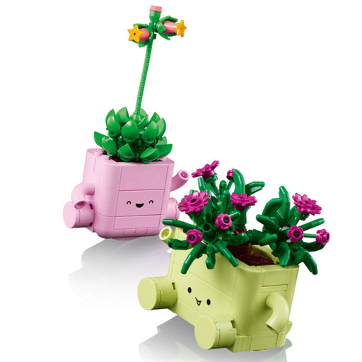 Two cute, block-style planter toys from LEGO on a clean white background. One pink planter holds a green succulent with a long green stem and small yellow flowers.