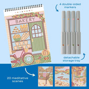 A spiral-bound craft journal featuring a colorful bakery illustration, shown alongside four double-sided markers in a light gray storage tray. Text on the image highlights '4 double-sided markers' and 'detachable storage tray,' with three small preview images at the bottom showing additional illustrated scenes.