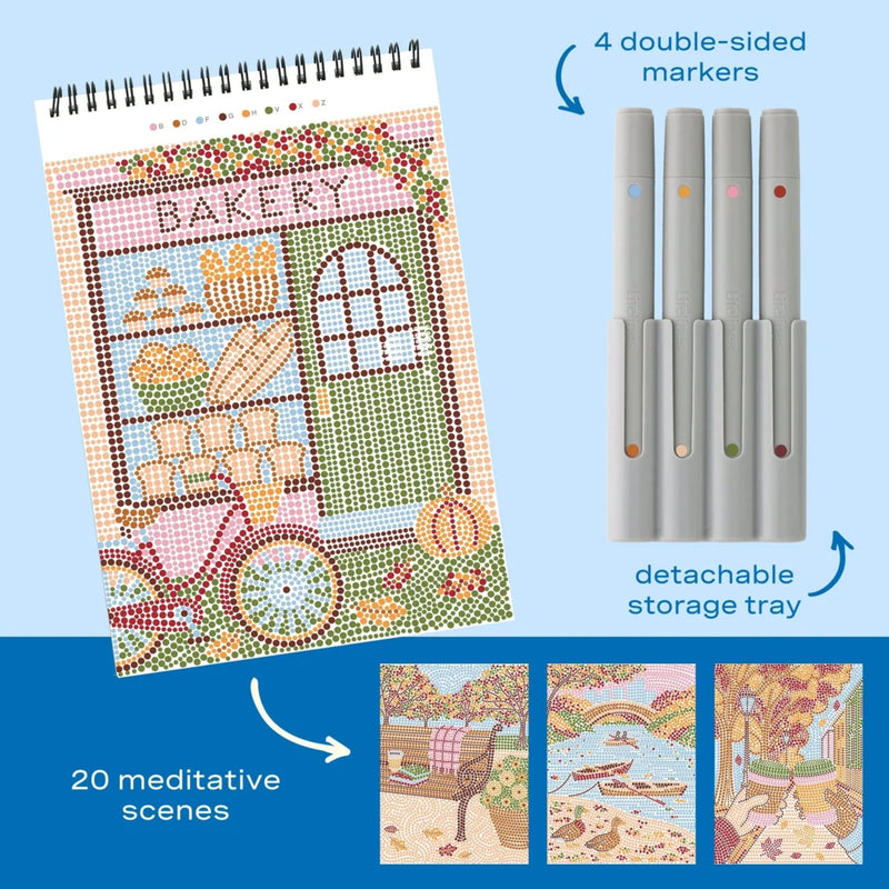A spiral-bound craft journal featuring a colorful bakery illustration, shown alongside four double-sided markers in a light gray storage tray. Text on the image highlights '4 double-sided markers' and 'detachable storage tray,' with three small preview images at the bottom showing additional illustrated scenes.