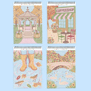Four spiral-bound art books or notebooks arranged in a 2x2 grid on a light blue background. Each features a colorful mosaic-style illustration: a gazebo with pumpkins, a coffee shop exterior, rain boots in a puddle with birds, and a bridge over water with swans.