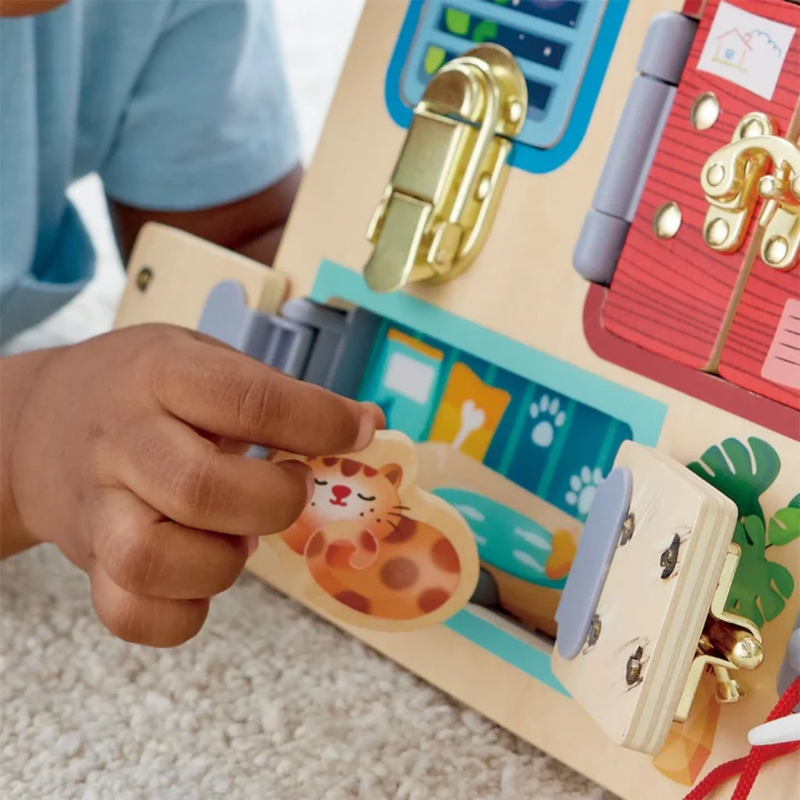 Child's hand interacting with Hape's Lock & Learn Playboard on a carpeted floor.