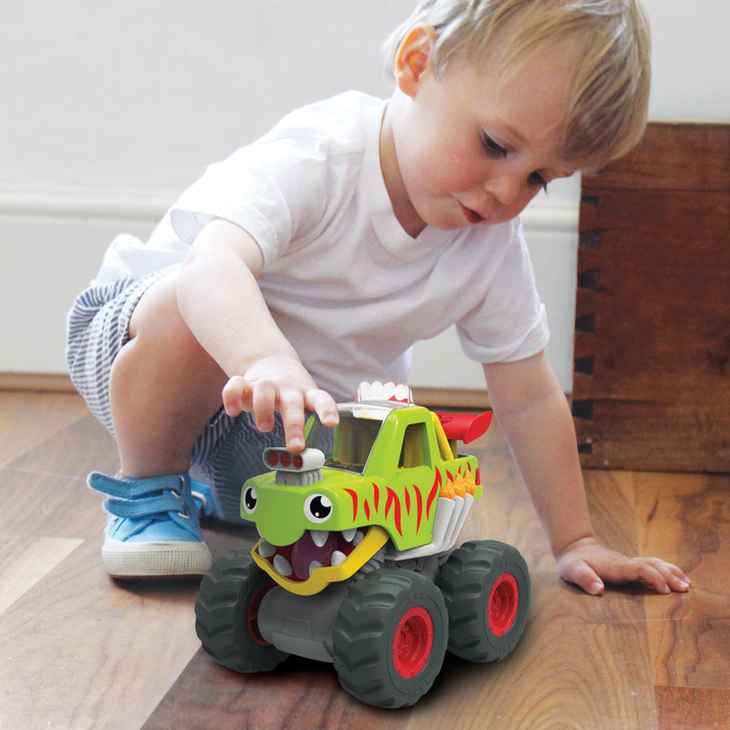 Toddler playing with green dinosaur-themed Mack Monster Truck toy on hardwood floor