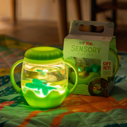 Lighted green sensory play jar with dragonfly and packaging on a colorful blanket.