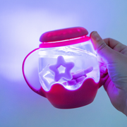 Hand holding the pink Glo Pals Mini Sensory Jar  (clear container with a star-shaped object inside), glowing with light.