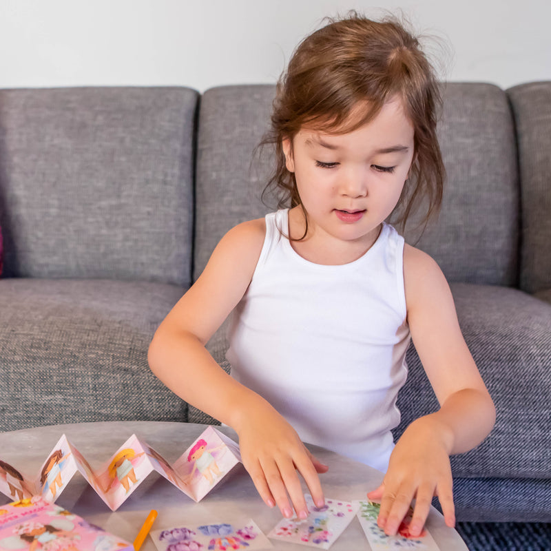Young girl playing with Mini Transfer Magic Flower Fairies on couch with colorful accordion book