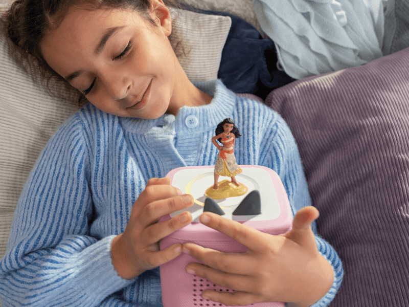 Child holding pink Toniebox with Disney Moana character figure on top in bedroom setting