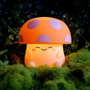 Cute mushroom-shaped night light with a orange cap and off white body on a grassy background.