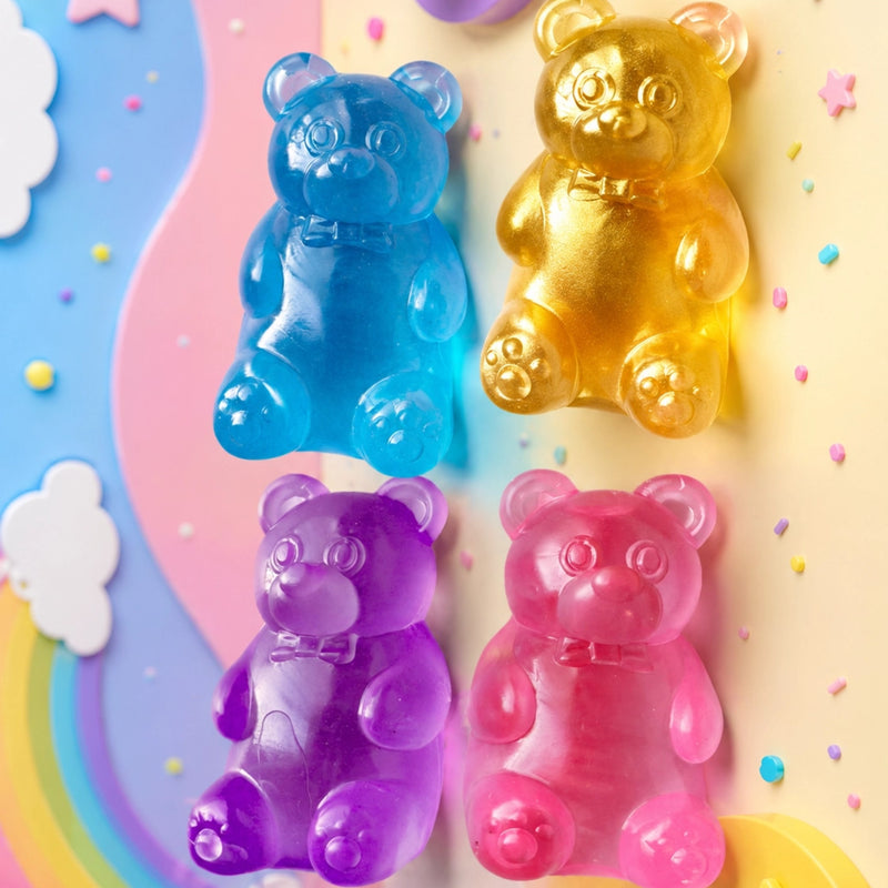 Four translucent teddy bear-shaped gummy candies in blue, gold, purple, and pink, arranged on a pastel decorative background with clouds, stars, and rainbow accents.