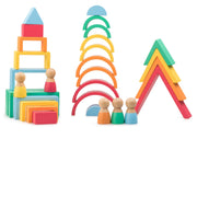 A set of colorful wooden children's blocks and shapes on a plain white background, including stacked rectangular and triangular blocks, arches, and small peg-doll figures.