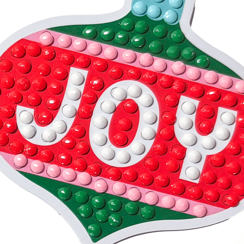 Close-up of JOY Christmas ornament-shaped sticker with colorful dot embellishments in red, green, pink, and white