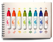 A set of eight Spot Color markers in assorted vibrant shades, lined up on a white spiral-bound notebook page with their corresponding color swatches and hand-drawn color swatches below each marker.