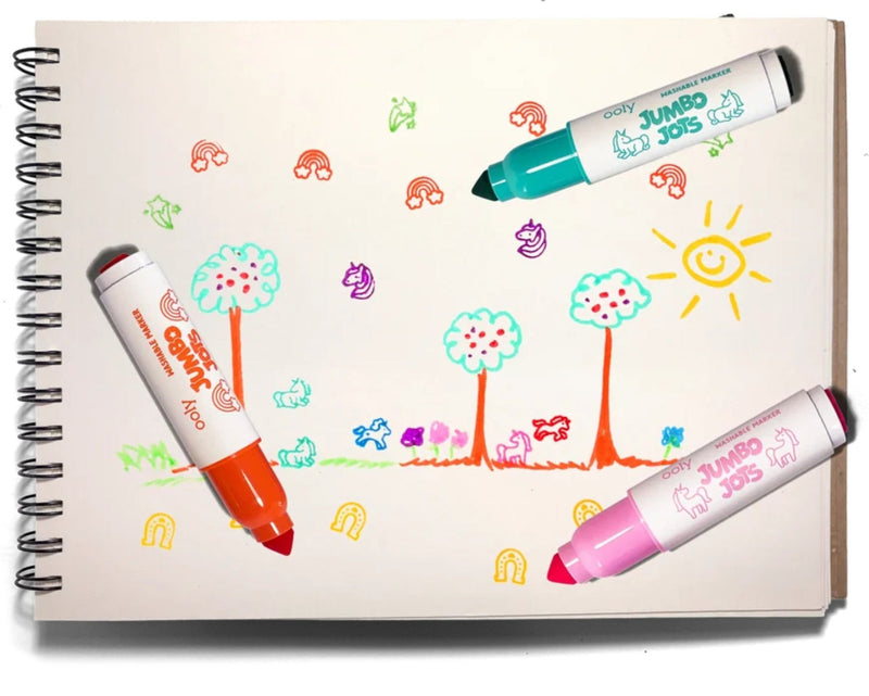 Three Jumbo Dot Kids dry-erase markers in orange, teal, and pink, laid on top of a spiral-bound children's drawing pad that shows colorful scribbled artwork.