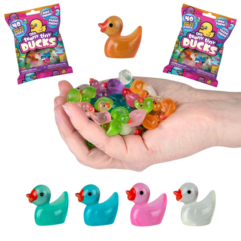 A hand holding a pile of colorful translucent duck-shaped beads or charms, with four small toy ducks shown along the bottom and two branded bags labeled 'Fuzzy Tiny Ducks' at the top left and top right. The background is plain white.